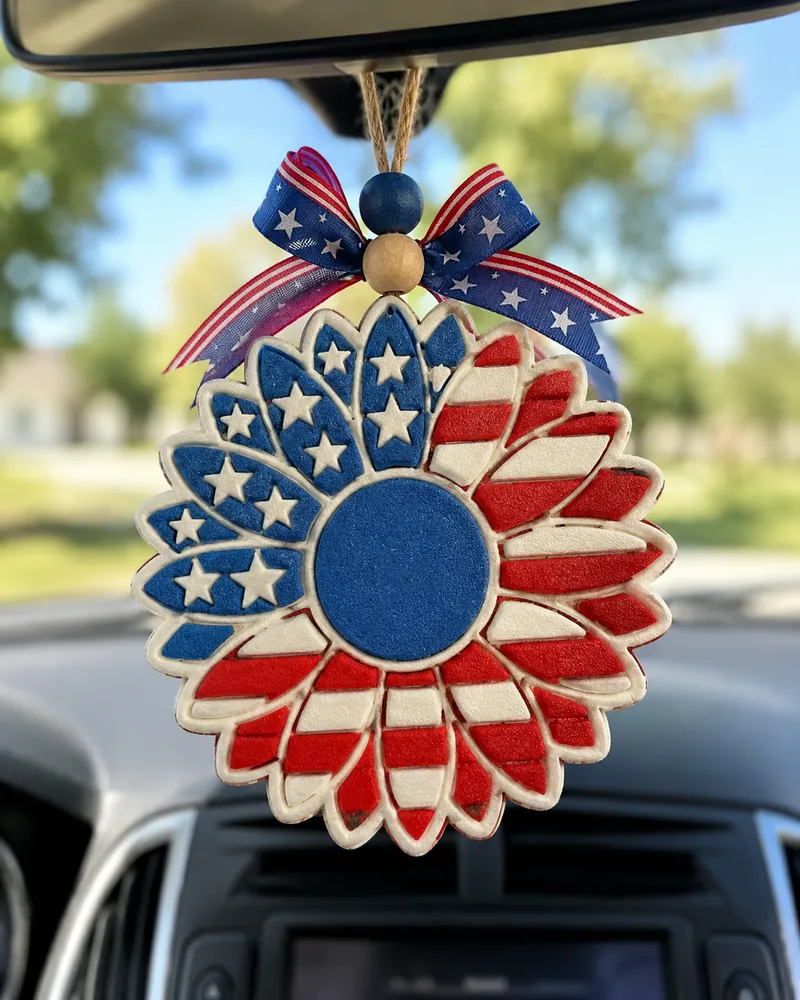Handmade American flag sunflower car freshie, a patriotic red white and blue aroma bead air freshener shaped like a sunflower, hanging from a car rearview mirror.
