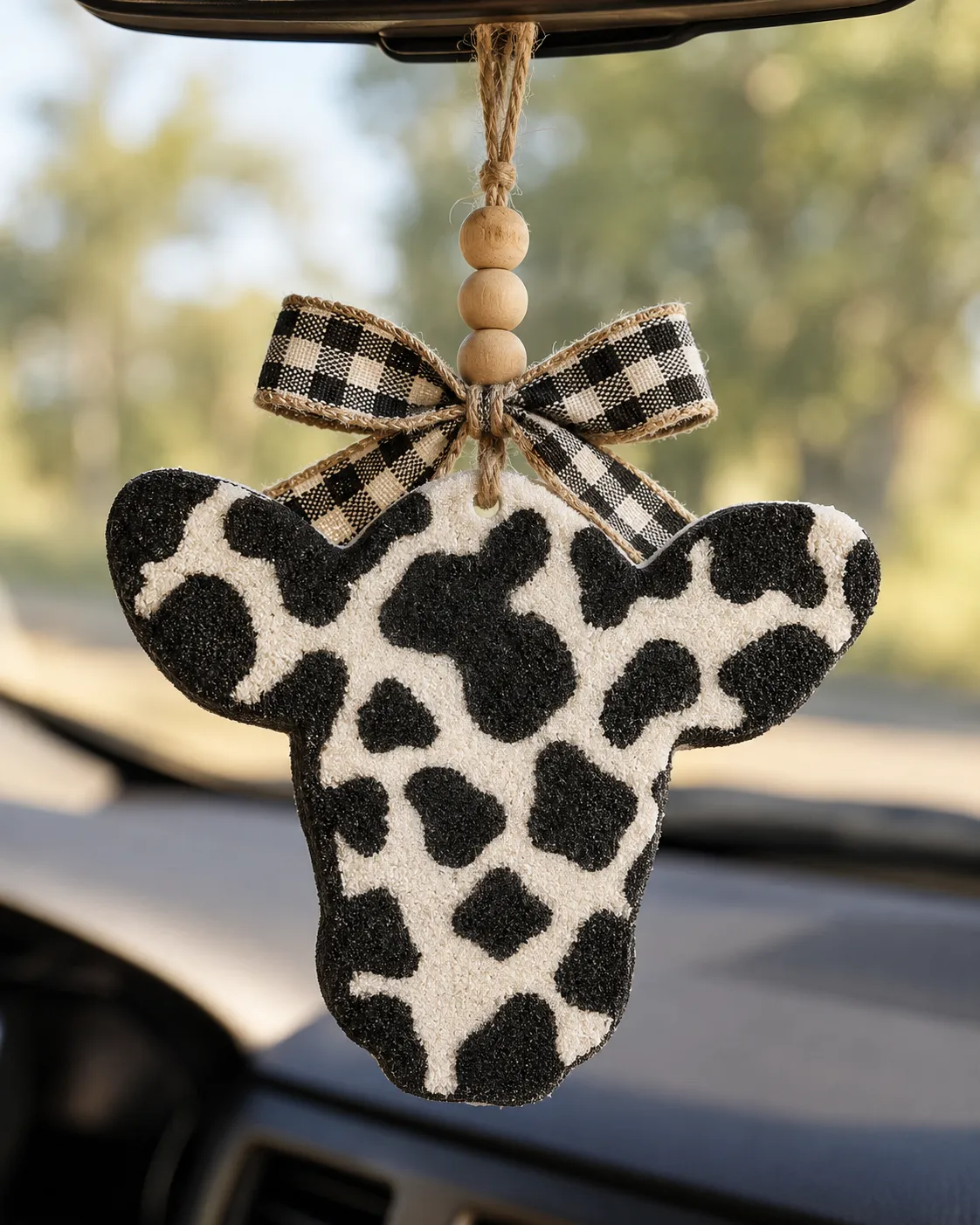 Handmade cow print cow head freshie, a western country scented aroma bead car air freshener hanging from a rear-view mirror.