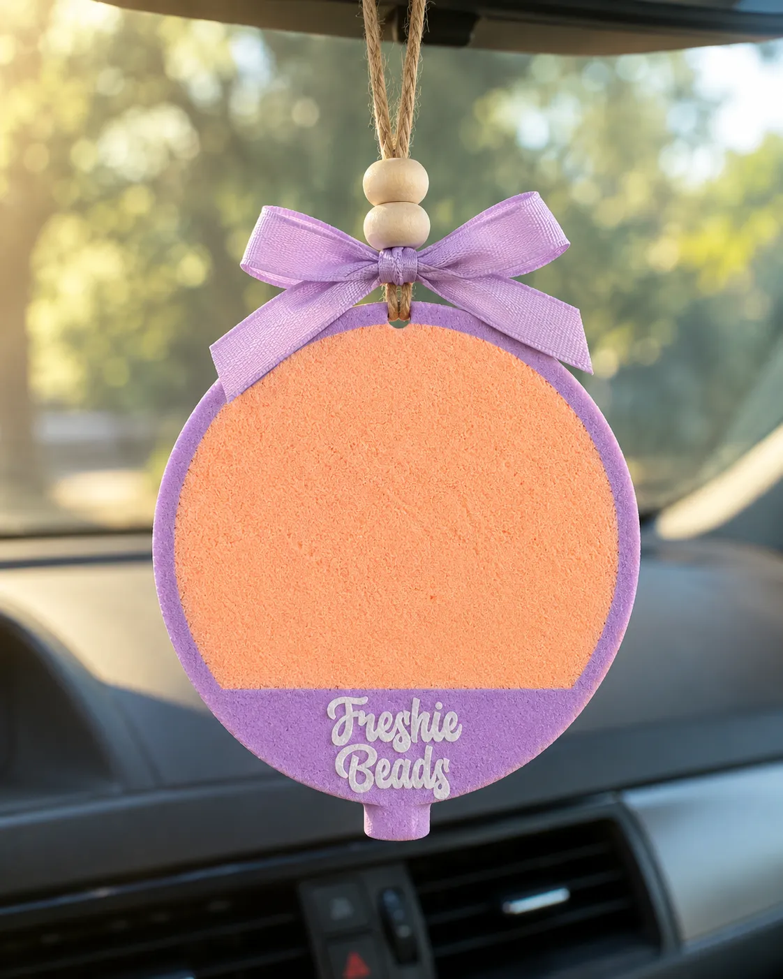 Round personalized car freshie with a custom name in cursive script, a handmade scented aroma bead air freshener for hanging on a car mirror.